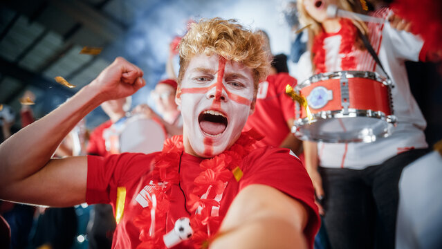Stadium Sport Event Selfie POV Camera App Portrait: Man with Painted Face Holding and Shooting Himself on Smartphone, Cheers for Red Team to Win, Screaming, Celebrating Championship Victory with Crowd