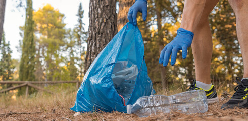 Detalle de brazos con bolsa de basura, recogiendo plástico en la montaña. - obrazy, fototapety, plakaty
