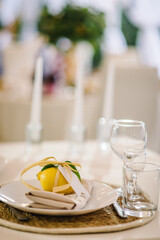 Banquet table served silverware, plate with napkin, cutlery and glasses. Wedding reception. Serving, setting table. Gift decorated with ribbons and branch greenery, decoration. Compliment for guests.