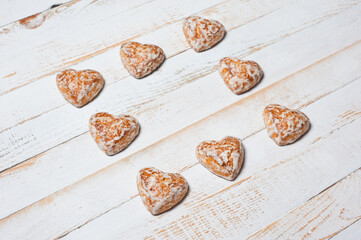 Sweet heart-shaped glazed gingerbread photographed on a white wooden surface.