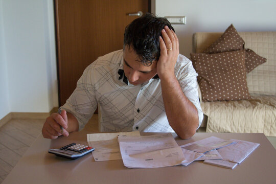 Image of a worried man using a calculator to calculate the bills that have just arrived. Increase in the cost of living due to the crisis.
