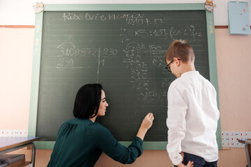 Maestra scrive con il gesso alla lavagna delle formule matematiche mentre lo studente guarda attento