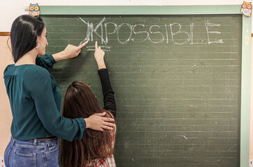 Insegnante mora con maglia verde indica insieme a una sua alunna  un punto nella  lavagna con sui...