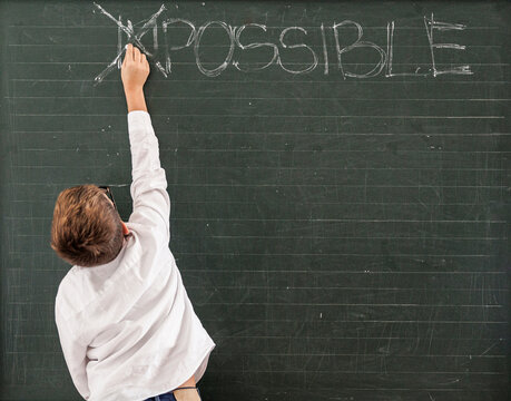 un bambino in punta di piedi cancella nella  lavagna le due lettere "IM" nella parola scritta " impossible", a indicare che tutto è possibile.