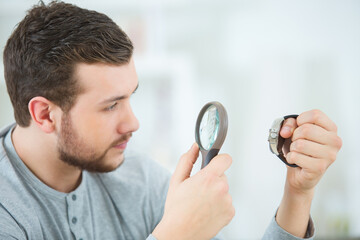 young man looking at watch through magnifying glass