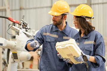 Female industrial engineer using remote control board to check robotic welder operation in modern...