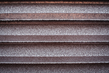 Brown metal fence covered with frost and ice crystals.