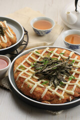 Homemade Okonomiyaki. Osaka flour dish with mayonnaise, spring onion, and sauce. Served on Ceramic Plate with Tea