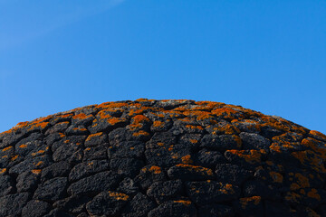 View of volcanic rocks from past volcano eruption on Lanzarote island. Round wall made of black rough texture lava stones and red lichen. Copy space with beautiful blue sky. Canary Islands, Spain.