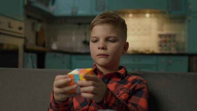 Kid Solving Cube Puzzle. Smart schoolboy playing with cube jigsaw sitting on couch at home.