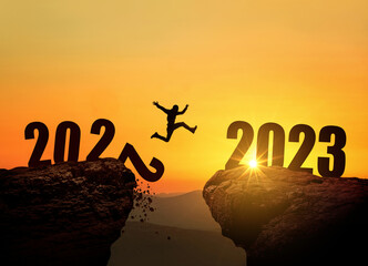 Man jumping on cliff 2023 over the precipice with stones at amazing sunset. New Year's concept....