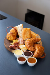 A delicious french breakfast set with croissants, baguette bread, jellies, butter and honey, cheese, brie, ham and parma on a wooden table in a nice home kitchen