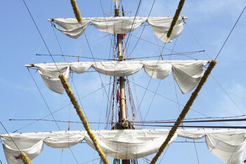 the mast of a large sailing ship with folded white sails against the sky, background