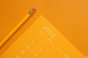 orange color 2023 year calendar and a pencil on table 