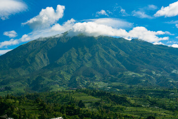 Fototapeta na wymiar The beauty of Mount Merbabu seen from Ketep Pass, a mountain covered with green hills and blue sky and a few clouds that spoil the eyes of visitors