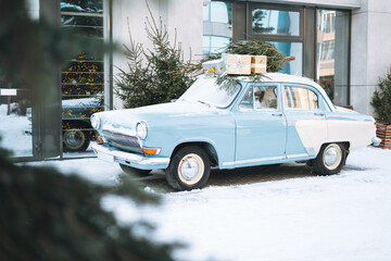 Vintage light blue car decorated with natural Christmas tree and boxes with gifts on winter street