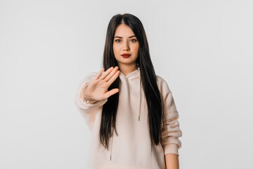 Stop it. Young woman making stop sign with hand, saying no, looking at camera, stands over white background. Serious girl with long hair disapprove smth, prohibit, taboo gesture