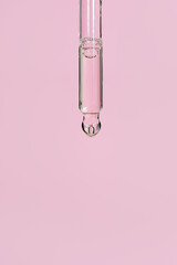 Transparent anti aging facial serum or oil in glass pipette on light pink background. Liquid gel...