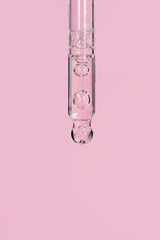 Transparent facial serum in glass pipette on light pink background. Liquid gel or essential oil...