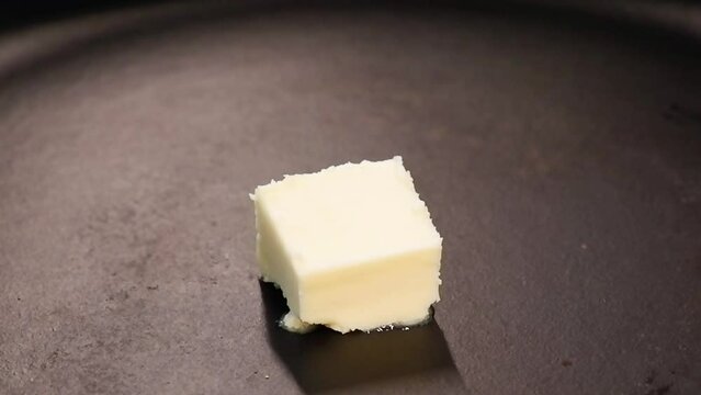 Piece pat of butter melting on a black cast iron frying pan, concept of cooking