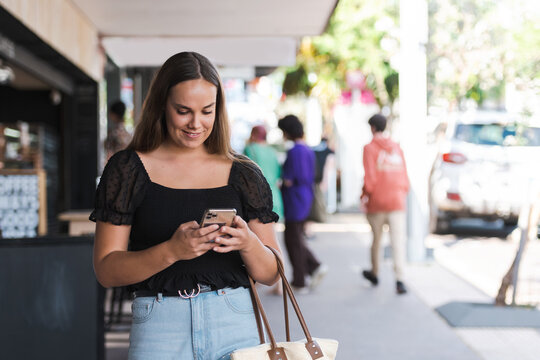 young woman walking in an urban setting, using her phone