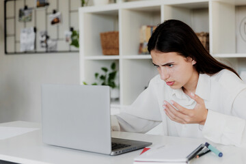 Angry young woman at home office desk work online on computer, have problems with device. Unhappy confused female distressed with laptop troubles, looks desperately, credit card issues while shopping