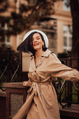 a brunette woman in a raincoat walks through the streets of the autumn city.