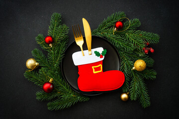 Christmas table with black plate, golden cutlery and holiday decorations.