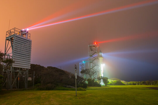 Beams of light from a lighthouse and beacon tower on a dark foggy night