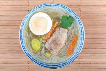 Top view of a plate with pork and funchose soup, with carrots, eggs and cilantro.
