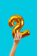 holds a balloon in the shape of the number 2