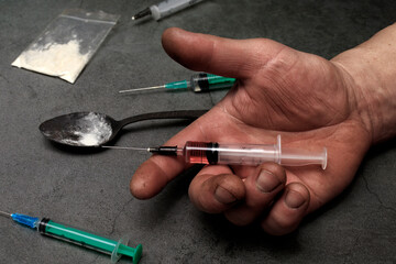 Syringe for injection in a man's hand. The hand holds the syringe. The concept of drug addiction, possession and distribution.