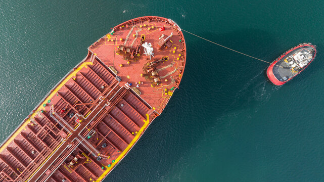 Aerial view of tug boat assisting big oil tanker. Large oil tanker ship enters the port escorted by tugboat.