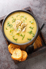 Creamy artichoke puree soup served with toasted bread close-up in a bowl on the table. Vertical top view from above