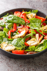 Fresh salad of artichokes, tomatoes, spinach, arugula, fried peppers and onions close-up in a plate on the table. Vertical