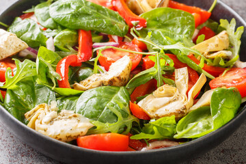 Delicious healthy salad of artichoke hearts, tomatoes, spinach, arugula, fried peppers and onions close-up in a plate on the table. Horizontal