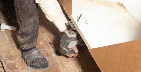 Worker cutting kitchen cabinet using electric saw.