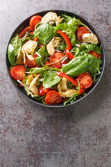 Fresh salad of artichokes, tomatoes, spinach, arugula, fried peppers and onions close-up in a plate on the table. Vertical top view from above