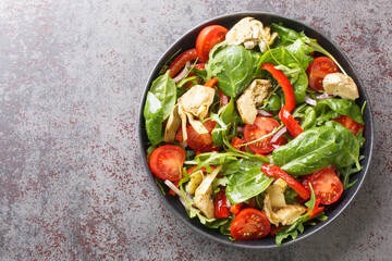 Fresh tasty salad of artichokes, cherry tomatoes, spinach, arugula, fried peppers and red onions close-up in a plate on the table. Horizontal top view from above