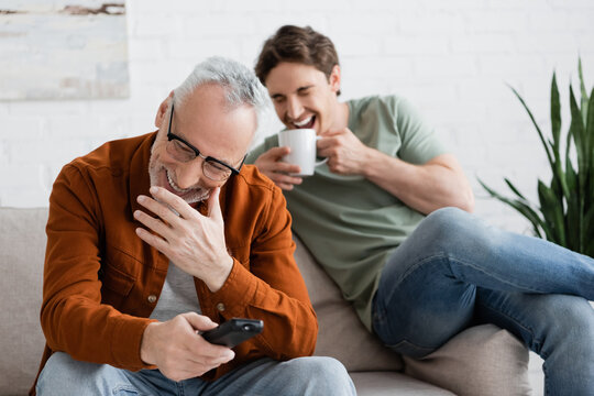 excited father and son watching comedy movie and laughing in living room