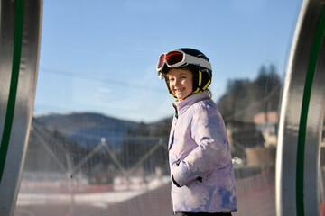 A girl on skis stands on a carpet ski lift in a glass tunel