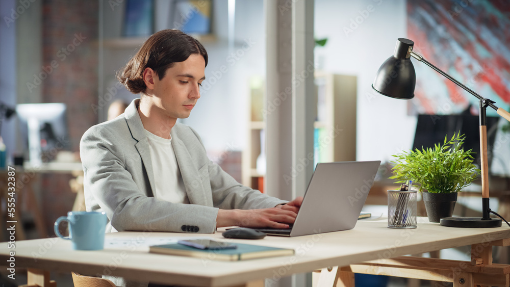 Poster handsome manager sitting at a desk in creative office. young stylish man in a jacket using laptop co