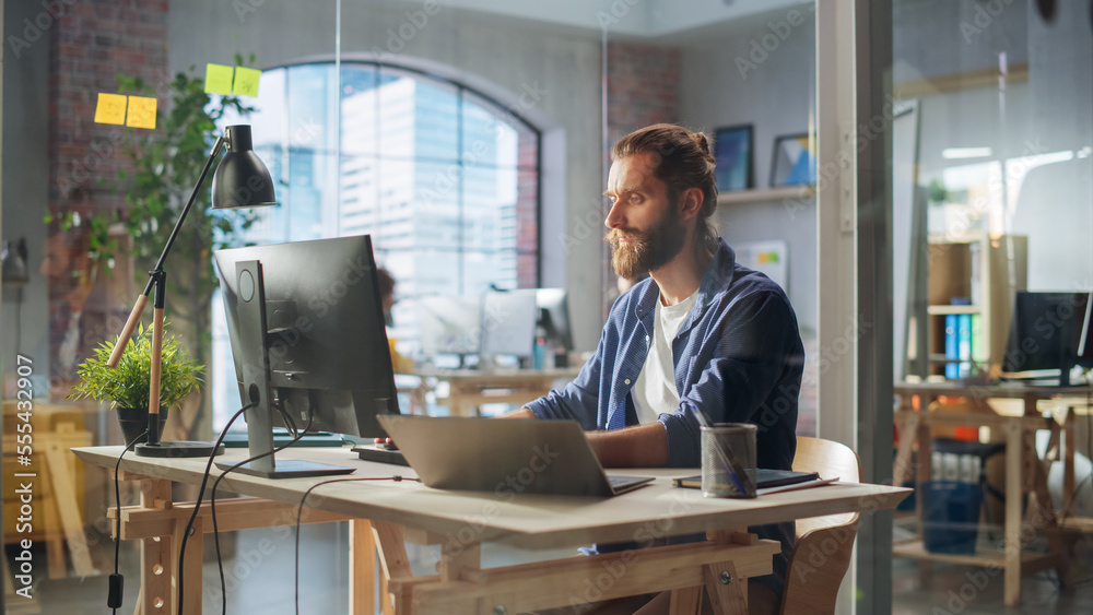 Aufkleber handsome long-haired bearded manager sitting at a desk in creative office. young stylish man using l