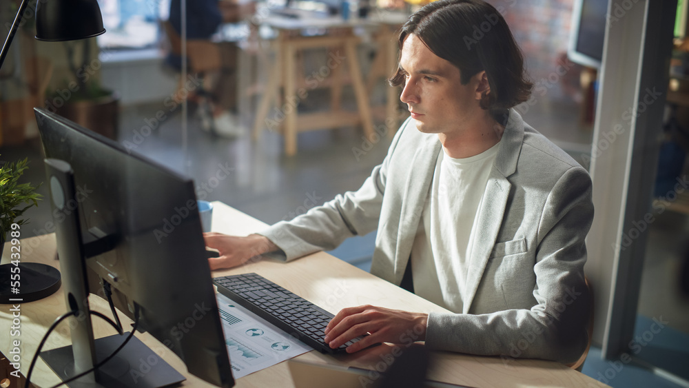 Poster stylish long-haired manager wearing a gray jacket, working at a desk in creative office. young hands
