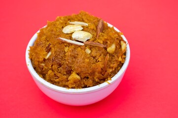 Closeup of Homemade Gajar Ka Halwa or Carrot Halwa Garnished with Almond Nut and Cashew Cuts in a White Bowl Isolated on Red Background