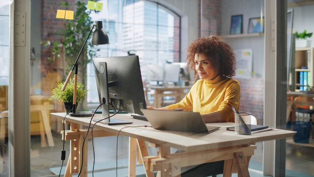 Close Up Portrait of a Happy Middle Eastern Manager Working in Creative Office. Young Stylish Female with Curly Hair Using Computer in Marketing Agency. Cinematic Footage Through a Glass Wall.