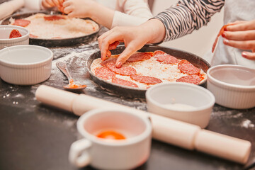 close up. children lay out pieces of salami on the basis of pizza.