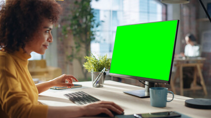 Portrait of an Excited Multiethnic Specialist Working in Creative Agency. Stylish Expressive Female in Yellow Jumper Using Desktop Computer with Green Screen Mock Up Display.