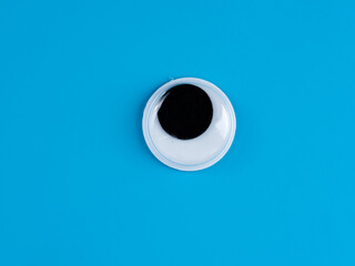 single wobbly googly eye isolated on a light blue  background with copyspace business logo - obrazy, fototapety, plakaty