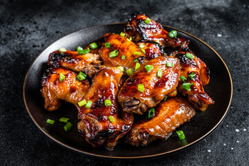 Baked chicken wings with sweet chili sauce in a plate. Black background. Top view